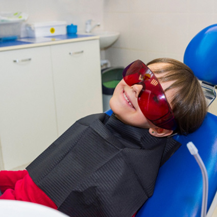 Boy smiling while wearing sunglasses and sitting in patient’s chair