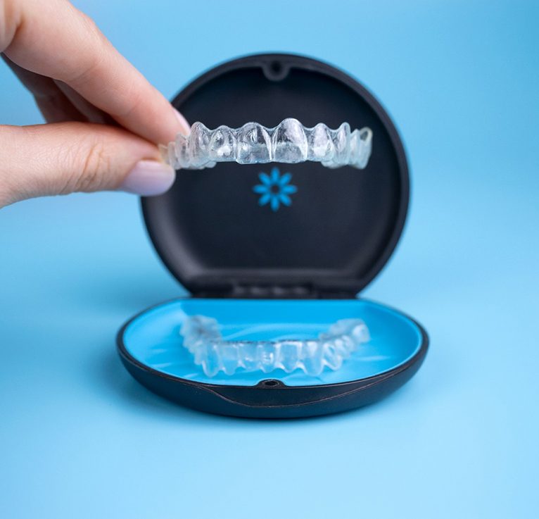 Invisalign tray being lifted from carrier case with blue background