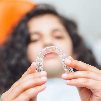 Girl in orange dental chair holding clear aligner