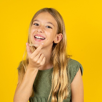 Girl holding clear aligner with yellow background