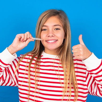 Girl in striped shirt holding Invisalign and giving thumbs up