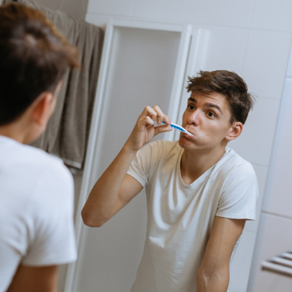 Teen brushing teeth with Invisalign aligners removed