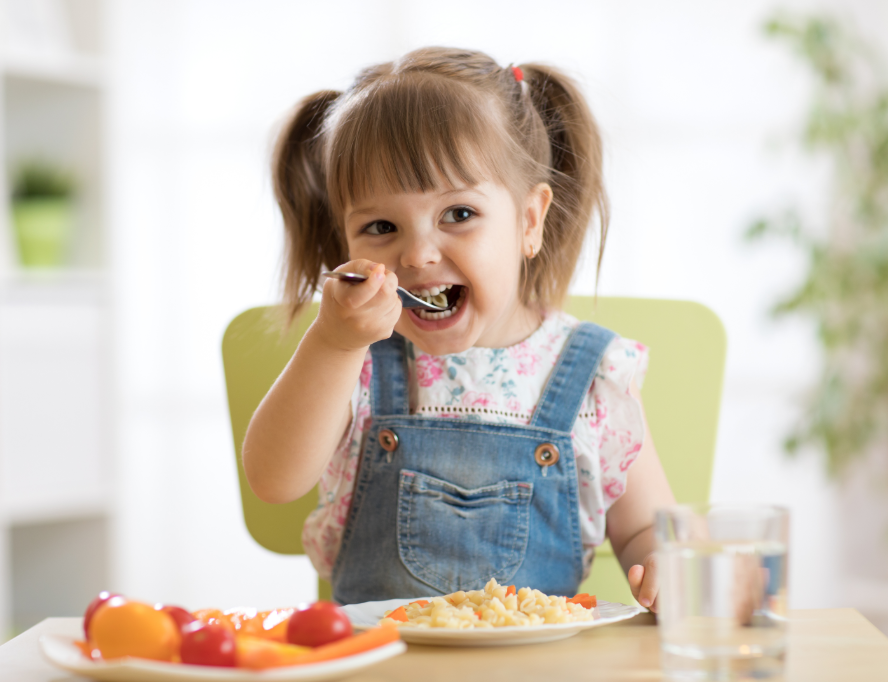 Little girl with pigtails and overalls eating healthy meal