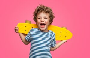 Smiling kid holding skateboard behind his back.